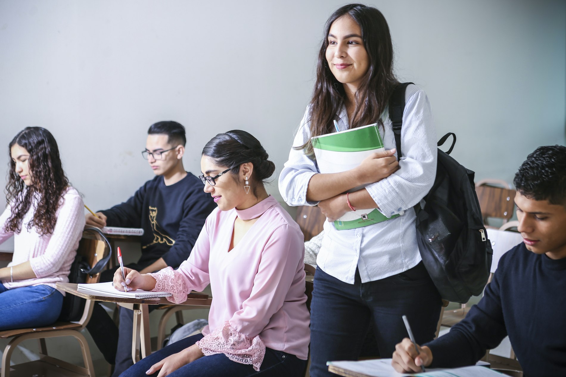 Estudiantes en clase, uno de ellos de pie con sus libros